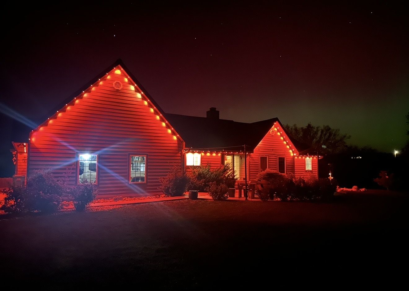 Country home washed in red permanent LED lighting under a starry sky